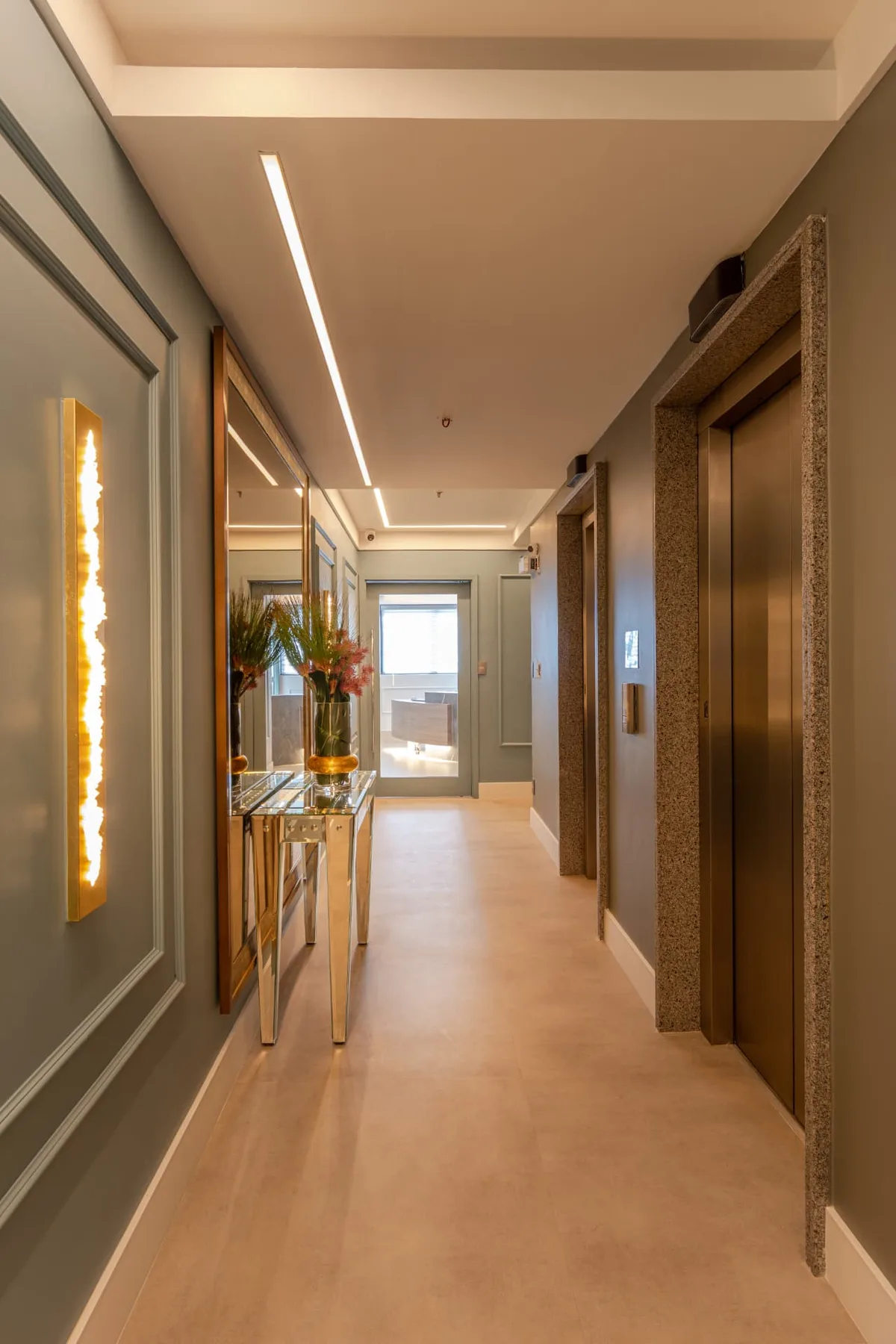 Corredor de entrada do consultório, com iluminação indireta e detalhes dourados